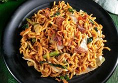 a black plate filled with noodles and vegetables on top of a green table cloth next to a fork