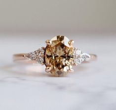 a yellow diamond ring with three white diamonds on the band and an oval shaped center stone