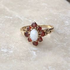 A vintage 9 carat gold white opal and garnet cluster ring. This beautiful piece holds a gorgeous collection of red stones in a gold setting, with a white opal in the centre. This piece is finished perfectly with twisted detailing down the shoulders.CONDITION: Wear consistent with age and use. Please see photos for more detail.ASSAYED IN LONDON APPROX. SETTING: 10mm x 12mmAPPROX. SETTING HEIGHT: 7mmAPPROX. BAND WIDTH: 1mmRING SIZE: UK: I | US: 4 1/4WEIGHT: 1.8 grams(VDZ) Beautiful Rings Vintage, Red Stones, White Sapphire Ring, Vintage Wedding Band, Gold Signet Ring, Opal Studs, Garnet Ring, Garnet Rings, Pretty Earrings