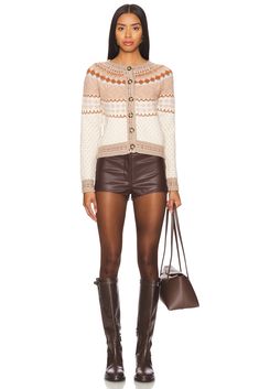 a woman in brown leather shorts and boots holding a handbag with her legs crossed