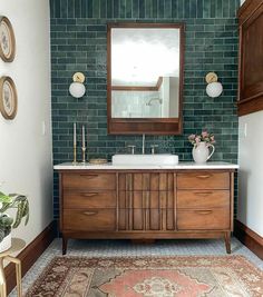 a bathroom with green tile and wooden cabinets in the corner, along with a rug on the floor