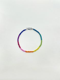 a rainbow bracelet with a silver beaded clasp on a plain white background the bracelet is made from glass beads and has a small metal charm