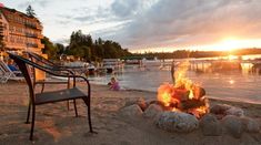 a chair sitting on top of a sandy beach next to a fire pit at sunset