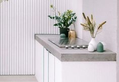 two vases with plants on top of a counter in a room that is white and has vertical striped walls