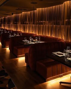 a dimly lit dining room with red velvet booths and long tables in front of a curtained wall