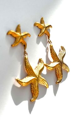 Dive into seaside charm with the "Starfish Earrings" – a delightful pair featuring a larger starfish dangling from a smaller one, both in radiant gold. These earrings capture the whimsy of the ocean, adding a playful touch to your style. Embrace the coastal allure with this charming accessory that evokes the beauty of starfish by the shore. 18k Gold Plated Nickel Free & Hypoallergenic Yellow Gold Starfish Earrings With Starfish Charm, Gold Star Charm Jewelry For Vacation, Elegant Yellow Gold Starfish Charm Earrings, Gold Jewelry With Star Charm For Vacation, Elegant Yellow Gold Earrings With Starfish Charm, Gold Starfish Jewelry For Vacation, Elegant Starfish Jewelry For Vacation, Yellow Gold Starfish Earrings For Gift, Elegant Starfish Shaped Jewelry For Vacation