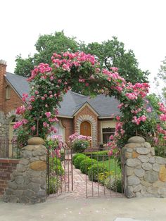 a stone fence with pink flowers on it and a house in the background