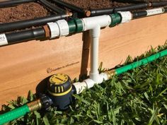 a garden hose connected to a wooden box filled with dirt and grass next to a green spigot