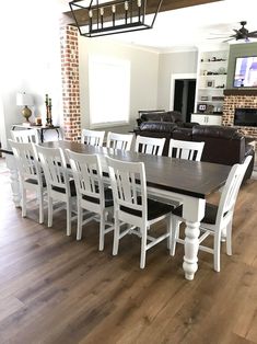 a dining room table with white chairs in front of a brick fireplace