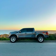 the truck is parked on the side of the road by the ocean at sunset or sunrise