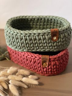 three knitted baskets sitting on top of a wooden table next to some dry grass