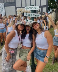 three girls are posing for the camera in front of a group of people wearing white shirts and hats