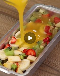 a plastic container filled with fruit and orange juice being poured on top of the salad