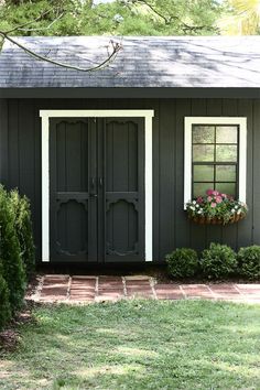 a small black shed with two windows and potted plants in the window sill