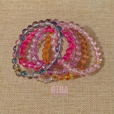 four bracelets with different colored beads on a beige cloth covered tablecloth, in the shape of letters o and o