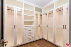 an empty walk in closet with glass doors and drawers on the wall, along with wood flooring