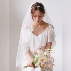 a woman in a white dress holding a bouquet of flowers and wearing a wedding veil