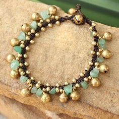 a close up of a bracelet with beads and green glass beads on a stone surface