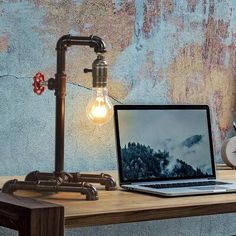 an open laptop computer sitting on top of a wooden desk next to a light bulb