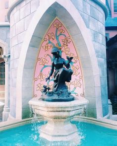 a fountain with a statue sitting on top of it in front of a pink and blue building