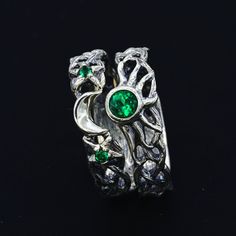 a silver ring with green stones and leaves on the outside, sitting on a black surface