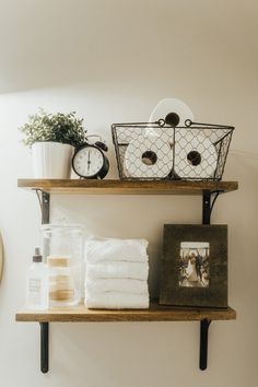 two shelves with towels, toilet paper and other items on them next to a clock