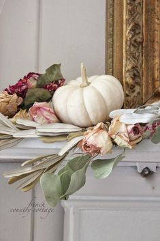 a white pumpkin sitting on top of a mantle next to dried flowers and greenery