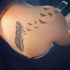 a woman's back with birds flying around her and a feather tattoo on it