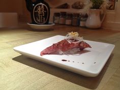 a white plate topped with meat on top of a wooden table next to a vase