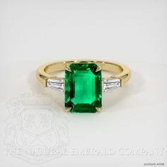 The ring features a beautiful, transparent 1.53 carat emerald shape green emerald with the dimensions of 9.00 x 6.75 x 3.53 mm and a emerald cut. It has a clarity grade of very slightly included (evaluated at eye level), intense color saturation, and an excellent polish. The origin of this emerald is Zambia. Also featured in the ring: White baguette (tapered) shaped diamonds, weighing approx 0.28 carats, clarity VS1/VS2 and a color grade of E. The ring is entirely set in 18K yellow gold. Three Stone Ring Settings, Green Emerald Ring, Bling Rings, Emerald Jewelry, Cut It, Three Stone Rings, Green Emerald, Baguette Diamond, Zambia