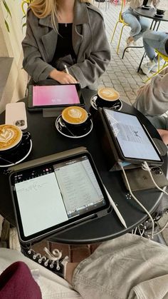 a woman is sitting at a table with two tablet computers and coffee cups on it