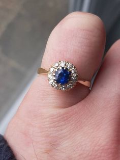 a person's hand holding a ring with a blue stone in it and diamond accents