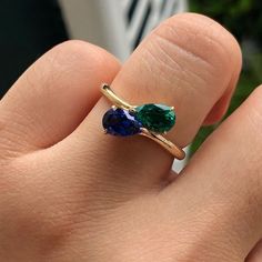 a woman's hand holding a ring with two green and blue stones on it