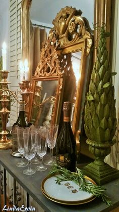 a table topped with lots of wine glasses next to a gold framed mirror and candlesticks