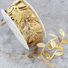 a spool of gold foiled leaves on a marble surface next to a pair of scissors