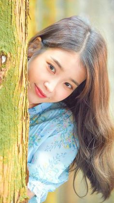 a young woman is posing next to a tree