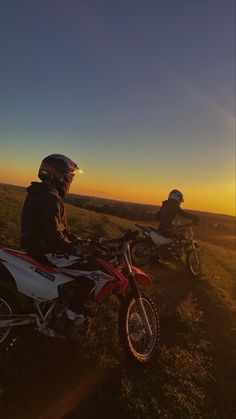 two people on motorbikes sitting in the grass at sunset, with one person wearing a helmet