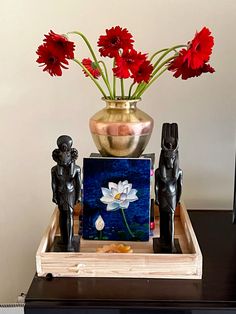 a vase with flowers in it sitting on top of a wooden table next to statues