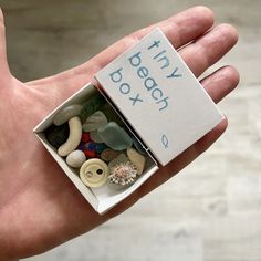 a hand holding a small box filled with different colored rocks and buttons that say tiny peach