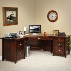 a corner desk with a clock and computer on it in front of a wall mounted painting