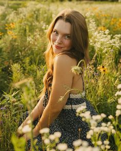 a woman sitting in the middle of a field with wildflowers and daisies