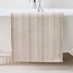 a white bath tub sitting next to a towel on top of a wooden floor in a bathroom