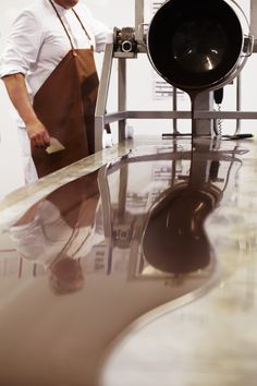 a man standing in front of a large pan on top of a counter next to a frying pan