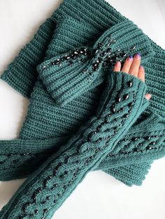 a woman's hand is wrapped up in a green knitted scarf with beads