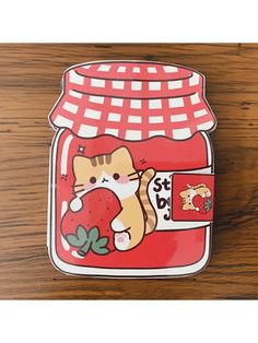 a red and white cat sticker sitting on top of a wooden table next to a jar