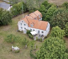 an aerial view of a white house surrounded by trees and grass with a red tiled roof