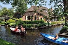 some people are in small boats on the water near a house with thatched roof