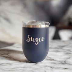 a blue cup with the word suzie on it sitting on a marble countertop