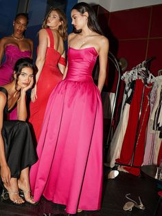 three women in dresses standing next to each other and looking at something on the floor