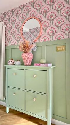 a green dresser with pink and white wallpaper in a room that has a mirror on it